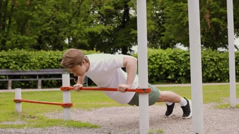 Young fit man performing incline pushups on a horizontal bar at an outdoor calis Stock Footage 336856351