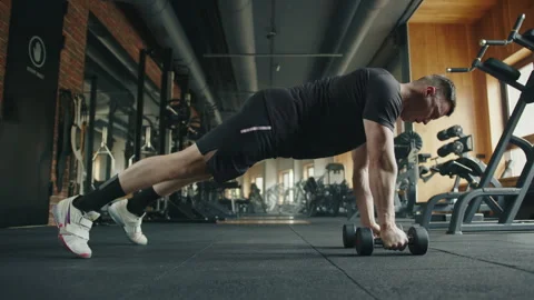 Young fit man performing push-ups exercises with dumbbells in gym Stock Footage 241492740