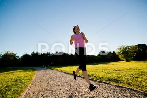 Young fit woman does running, jogging training in a park at summer sunny day Stock Photos