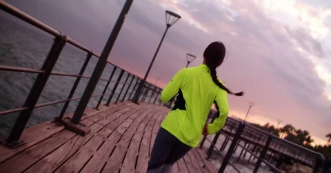 Young fit woman running next to the sea at sunset Stock Footage