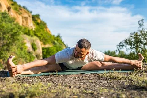 Young fitness man doing yoga exercise outdoors at the quarry lake. Handsome y Stock Photos