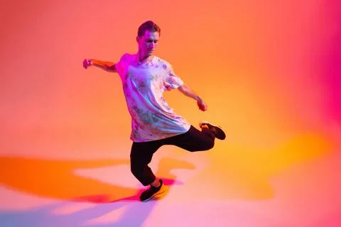 Young flexible boy dancing hip-hop isolated over gradient yellow pink studio Stock Photos