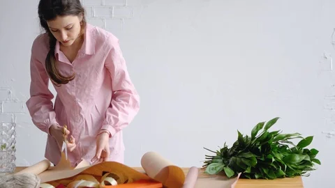 A young florist prepares paper for packaging flowers Видео 85929999