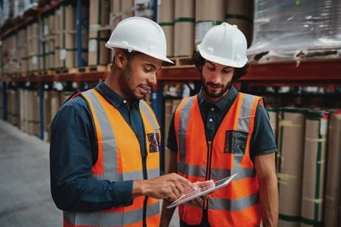 Young focused workers in warehouse discussing work on digital tablet Stock Photos