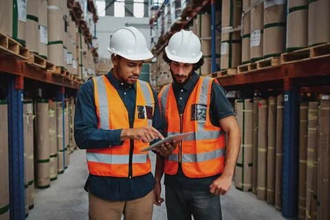 Young focused workers in warehouse discussing work on digital tablet Stock Photos