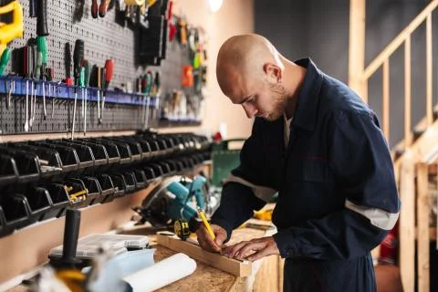 Young foreman in work clothes thoughtfully using measuring tape Stock Photos