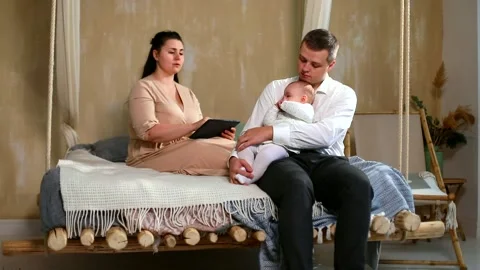 Young freelance mother using tablet at home talking with husband playing with 스톡 동영상 147133555