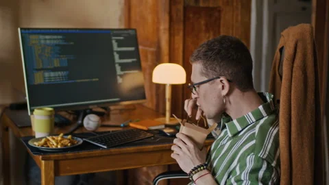 Young Freelance Programmer Coding on Computer and Eating Noodles at Home Stock Footage 334804716