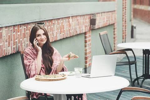Young freelancer communicates using smartphone while eating pizza in cafe Stock Photos