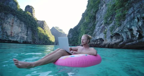 Young freelancer male floating on inflatable remote working anywhere on laptop. Stock Footage 149660596