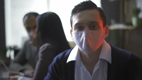 A young freelancer in a protective mask works in the office with colleagues who Stock Footage 130577277