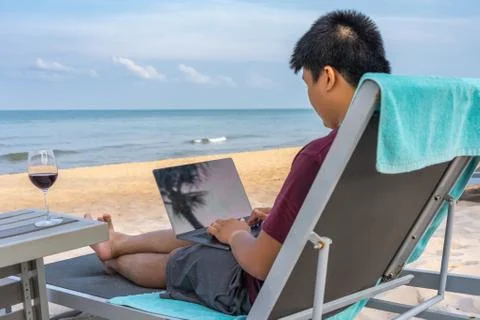 Young freelancer using laptop beside glass of wine on beach Stock Photos