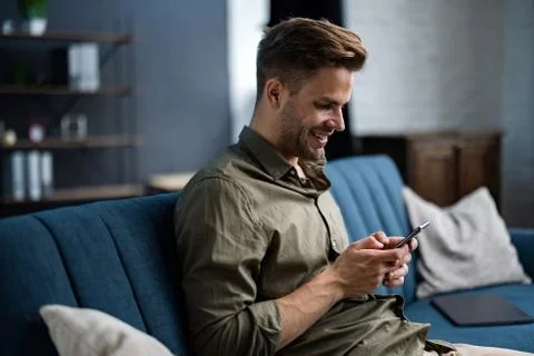 Young freelancer using smartphone and smiling. Happy man using mobile phone apps Stock Photos