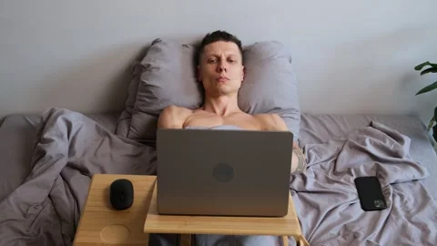 Young freelancer working in bed, happily dancing to music while using laptop Video stock 314430354