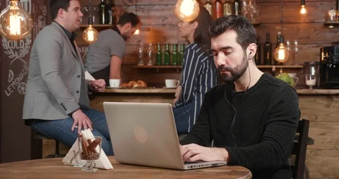 Young freelancer working at his laptop being served coffe and croissant at Stock Footage 103369983