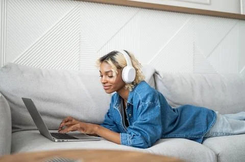 Young freelancer working at home lying on the couch. Student girl watching Stock Photos