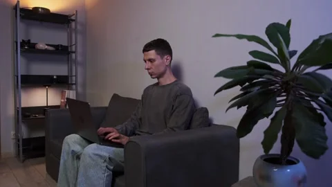 Young freelancer working on laptop sitting on sofa home authentic lifestyle Vídeo Stock 315413998