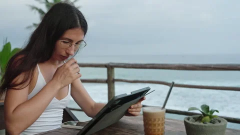 Young freelancer working on tablet at cafe with ocean view, palm trees. Female Stock Footage 252395430