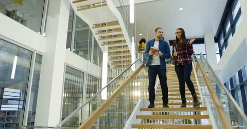 Young friendly couple of groupmates walking down the stairs at the college after Stock Footage 83717456