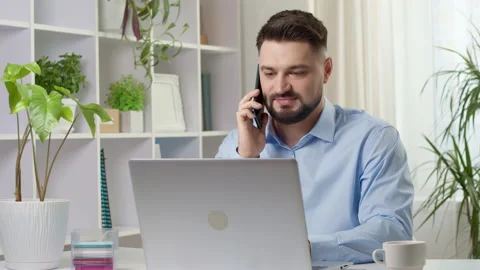 A young friendly man with a beard sitting in the office talking on a phone Stock Footage 169600650