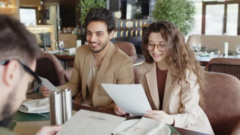 Young friends choosing food from menu while sitting at cafe table Stock Footage 252199026
