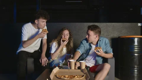 Young friends eats pizza and talks in dark room Stock Footage 136372873