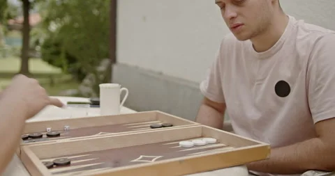 Young friends enjoying a game of backgammon outside. A casual and relaxing scene Stock Footage 281578606