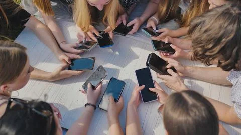 Young friends gather in a circle, using their smartphones to stay connected in Stock Photos
