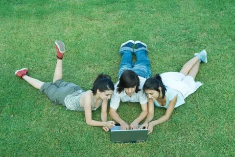 Young friends lying in grass, using laptop together Stock Photos