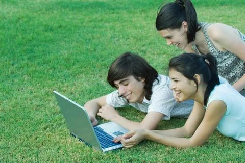 Young friends lying in grass, using laptop together Stock Photos