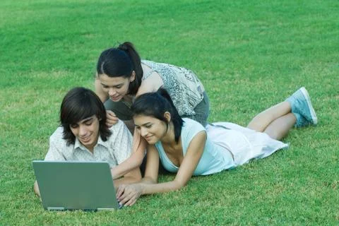 Young friends lying in grass, using laptop together Stock Photos