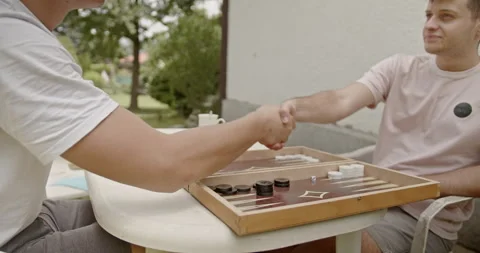 Young friends playing backgammon outdoors in a garden on a sunny day. Engaged in Stock Footage 281967446