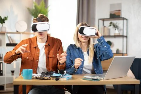 Young friends sitting at the table with VR headset and enjoying 3D reality Stock Photos