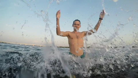Young funny happy guy standing in the river's water and splashing on camera at 库存影片 114667947