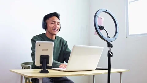 Young game streamer using laptop and headphones with ring light setup for Stock Footage 320429497