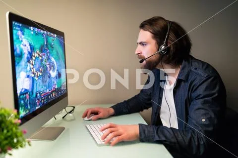 Young Gamer In Headphones Using Computer For Playing Game At Home