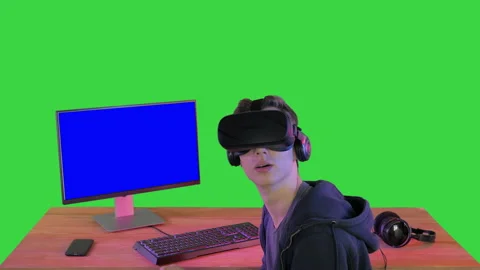 Young gamer in virtual reality headset sitting at table on a Green Screen Stock Footage 136477265