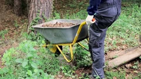 Young gardener in work overall walking with wheelbarrow Stock Footage 130659835