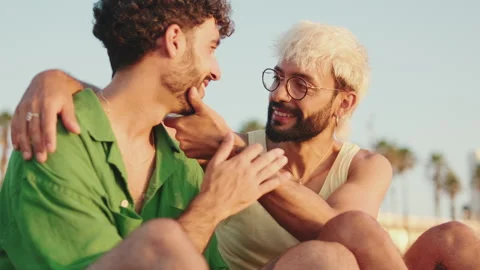 Young gay couple hugging while sitting on the beach Stock Footage 250841255