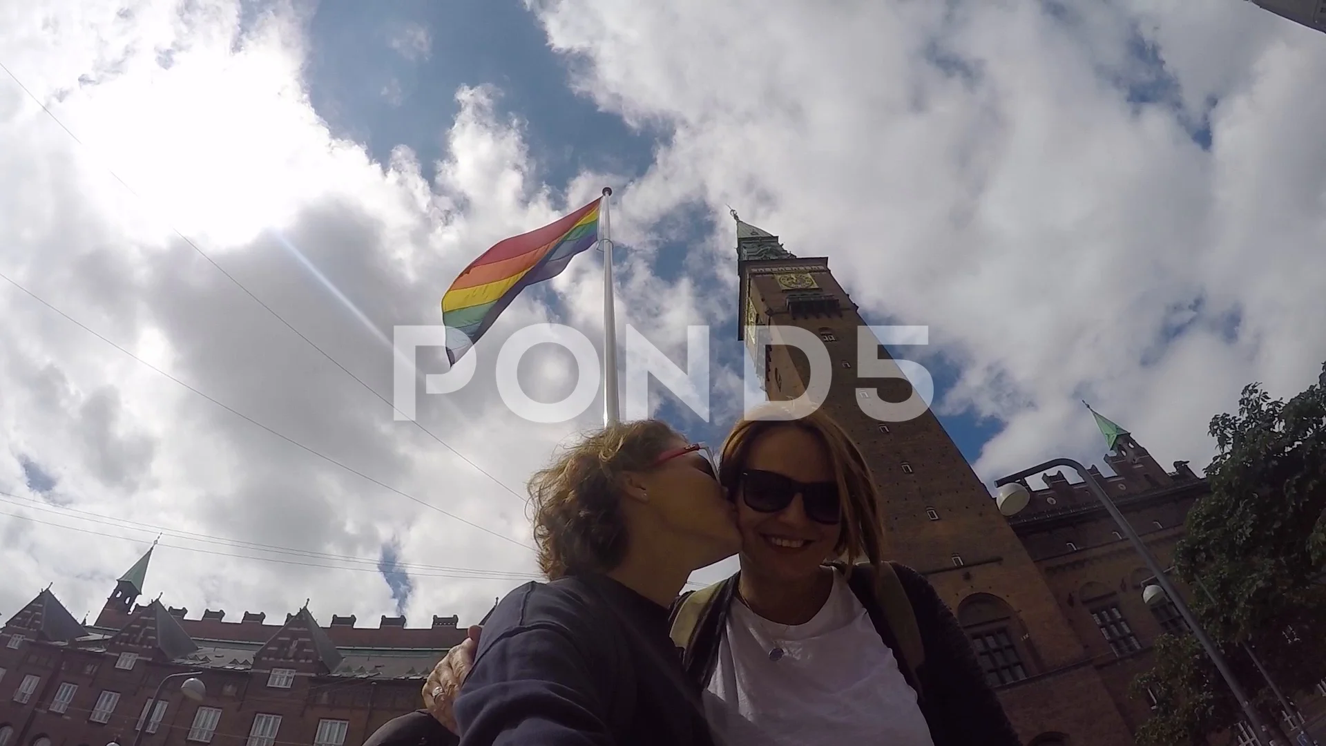 A young gay couple is kissing on the background of the swinging rainbow  flag.