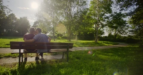 Young Gay Couple Sitting On A Bench In The Sun Stock Footage