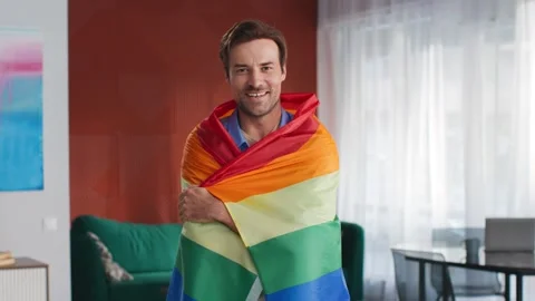 Young gay man looking at camera holding rainbow flag Stock Footage 243640423