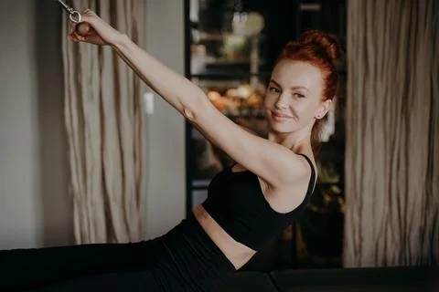 Young ginger female smiling while doing exercises on pilates reformer Stock Photos