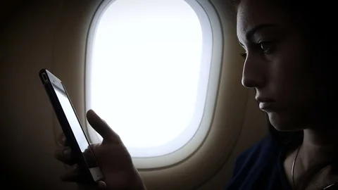 Young gir is using a smartphone inside an airplane near window Stock Footage 83325259