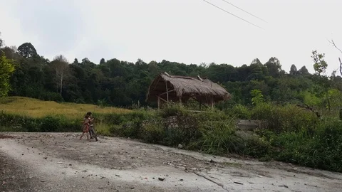 Young girl with baby strapped to back holds bike next to wooden hut, Houaphan Stock Footage