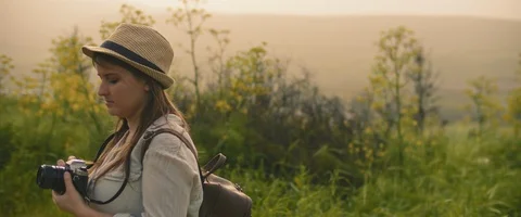 A young girl with backpack and a hat taking pictures of landscape at sunset Stock Footage 127099715