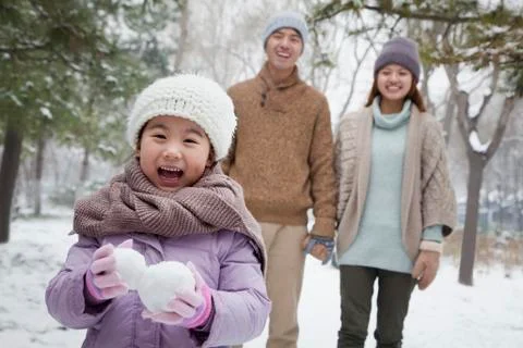 Young girl carrying snow balls in front of parents in park in winter Stock Photos