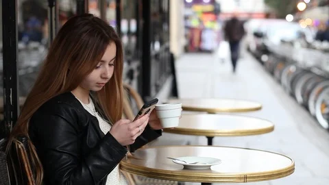 Young girl checking emails and messages online on her phone in cafe in Paris Stock Footage 98093540