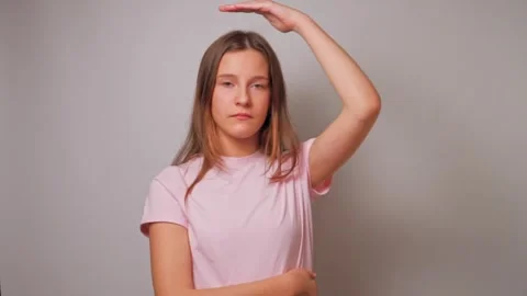 Young girl checking her height by raising hand and looking up playfully on white Stock Footage 311959694
