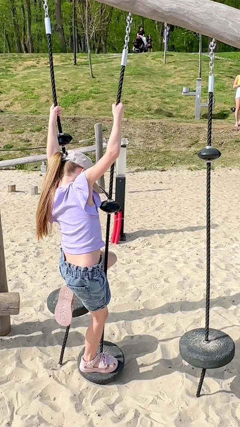 Young girl climbs on a playground structure by a lake, with a sandy beach Stock Footage 340653858
